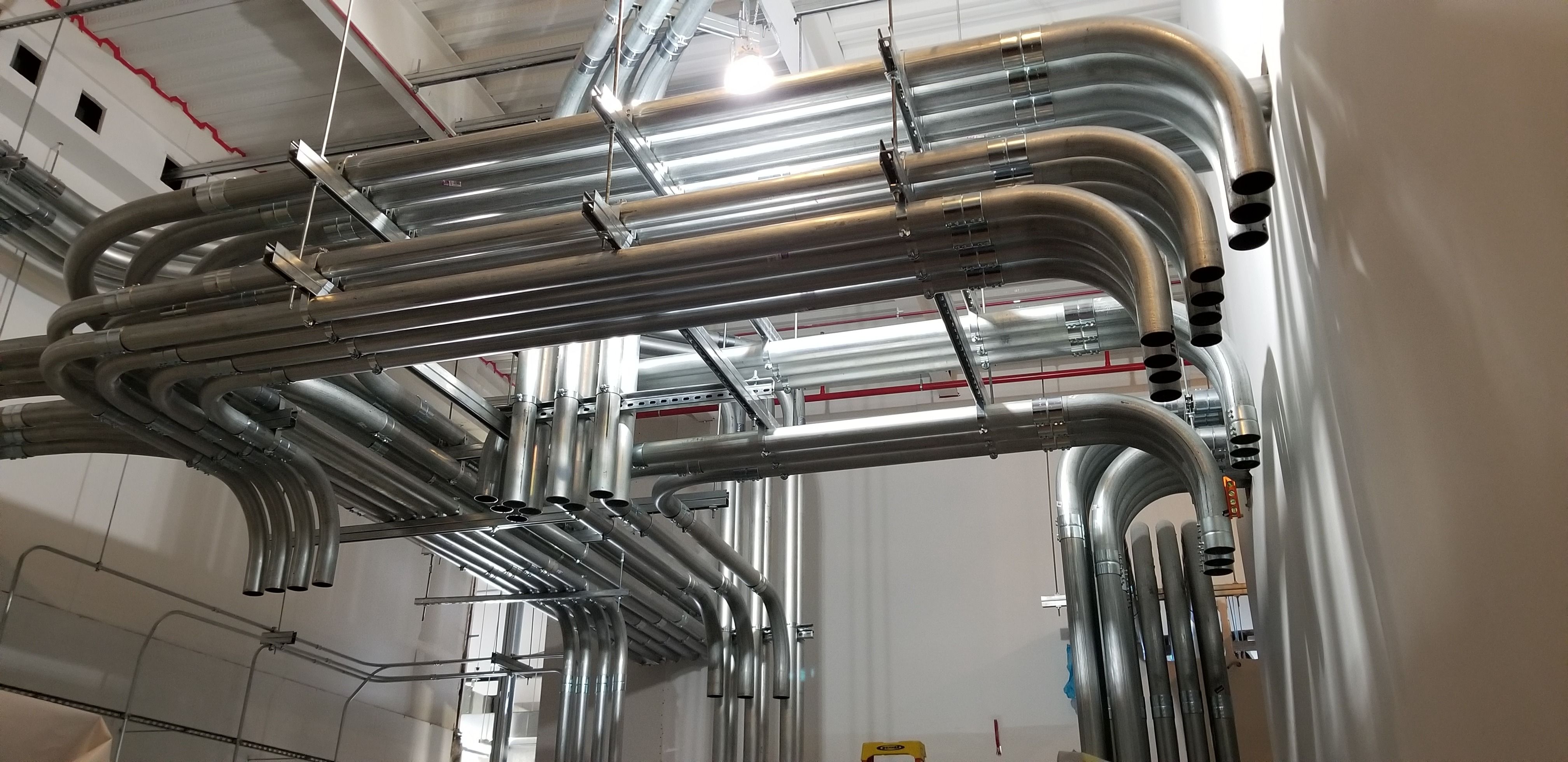 Parallel runs of steel conduit with matched sweeping bends, racked overhead on a commercial project