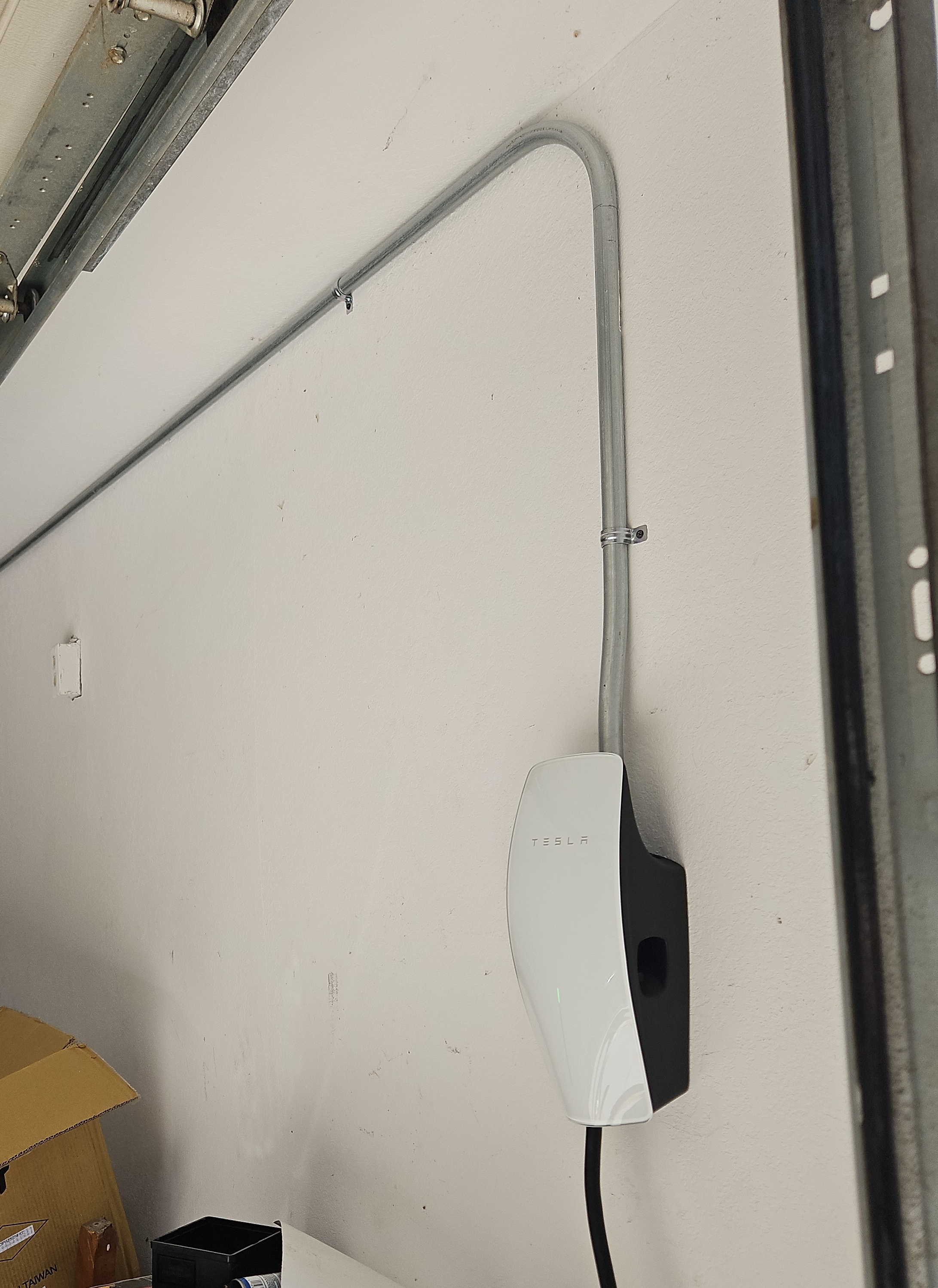 Wall-mounted EV charger in a residential garage fed by surface conduit